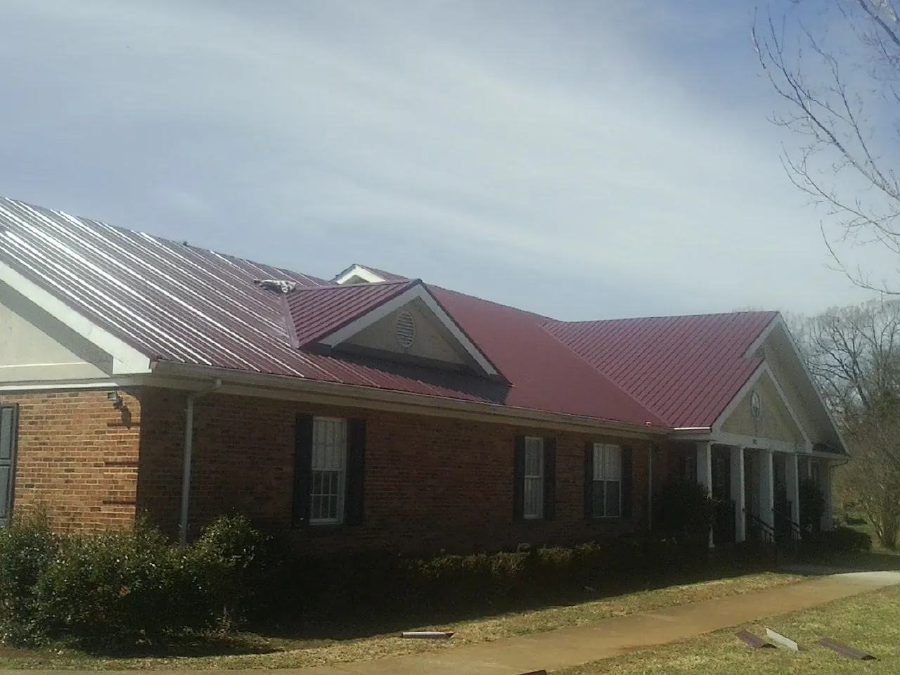 Red metal roof with gabled entries on a long brick building, from a Hail Damage Roof Repair job in Port Angeles