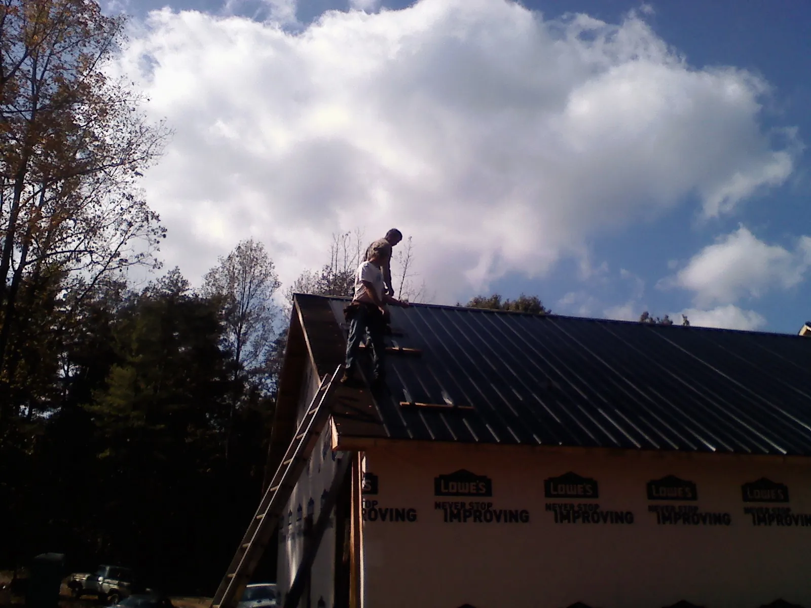 Roofer fastening dark metal panels high against a cloudy sky, from a Roof Inspection job in Port Angeles