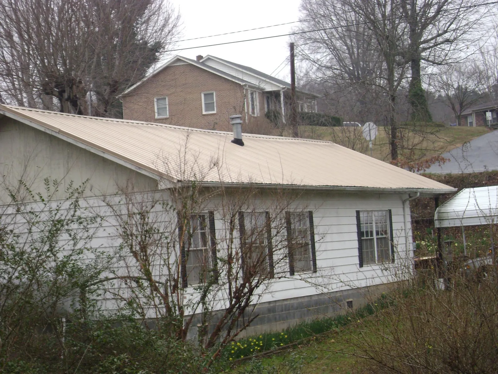Tan metal roof on a white sided house set into a hillside in Port Angeles